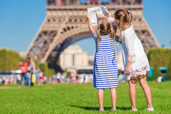 Duas meninas com um mapa em frente à Torre Eiffel com roupas de verão aproveitando a Europa em julho