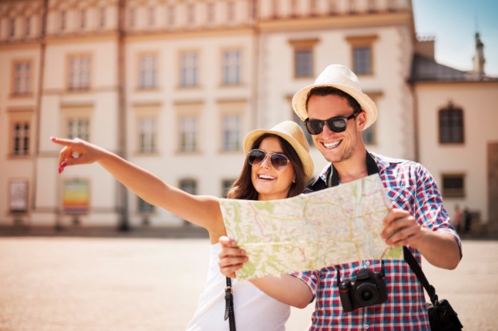 Casal sorridente com um mapa na mão e roupas de calor para desbravar a Europa no verão em sua lua de mel