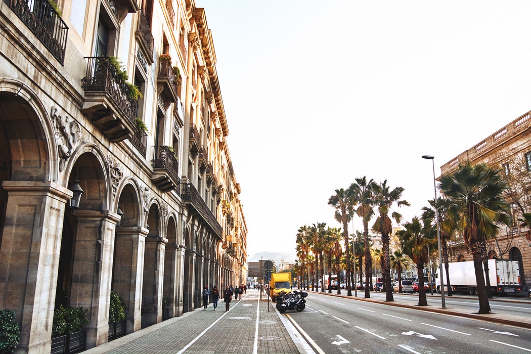 Barcelona e sua rua com palmeiras e construção arquitetônica, ideal cidade para ser visitada em uma excursão para Europa